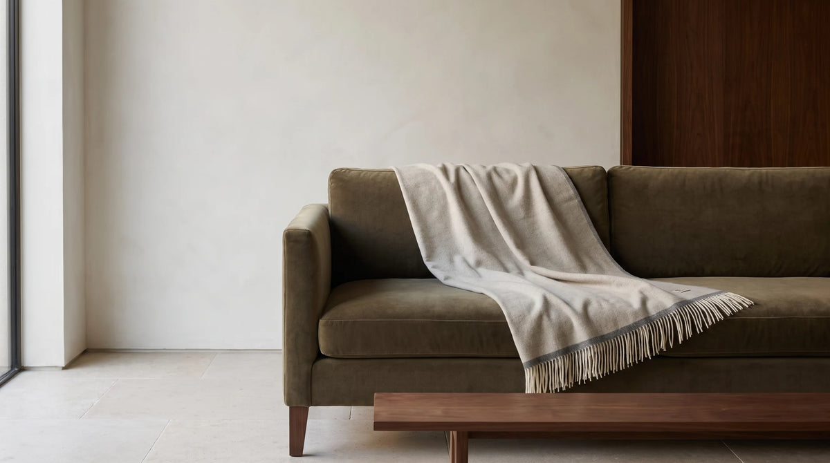 Plaid Milano Beige sur un canapé olive, dans un intérieur minéral au mobilier en noyer.