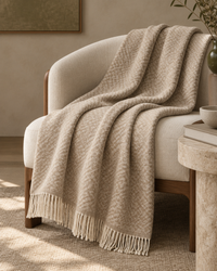 Mise en scène du plaid Kentii sur un fauteuil en bois et lin, avec son motif beige et ses franges écrues
