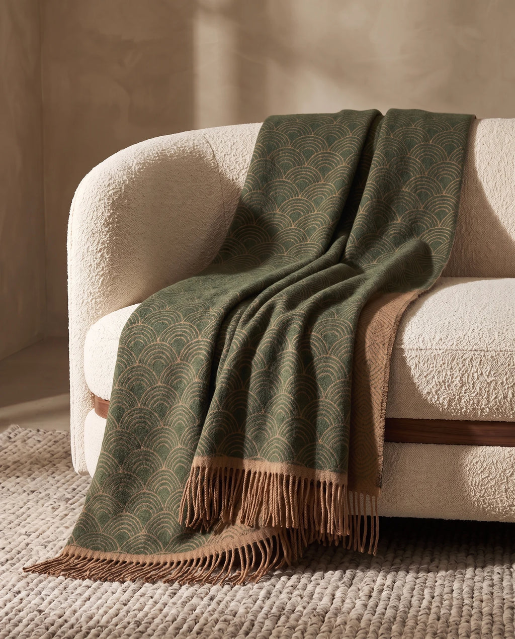 Plaid Venezia Feuille vert et camel, drapé sur un canapé crème — mise en scène